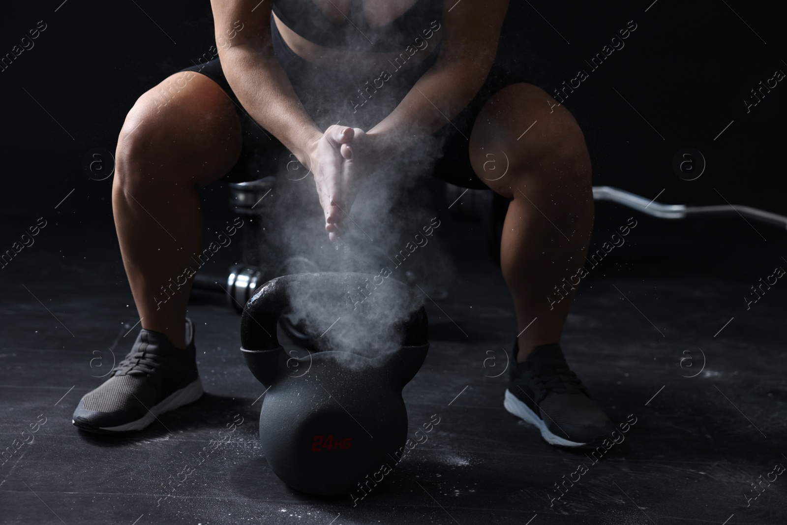 Photo of Woman clapping hands with talcum powder before training with kettlebell on black background, closeup