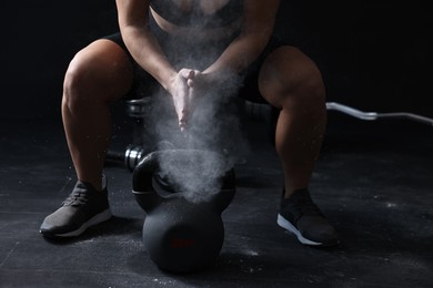 Photo of Woman clapping hands with talcum powder before training with kettlebell on black background, closeup