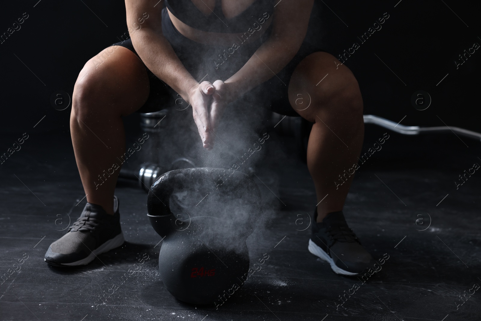 Photo of Woman clapping hands with talcum powder before training with kettlebell on black background, closeup