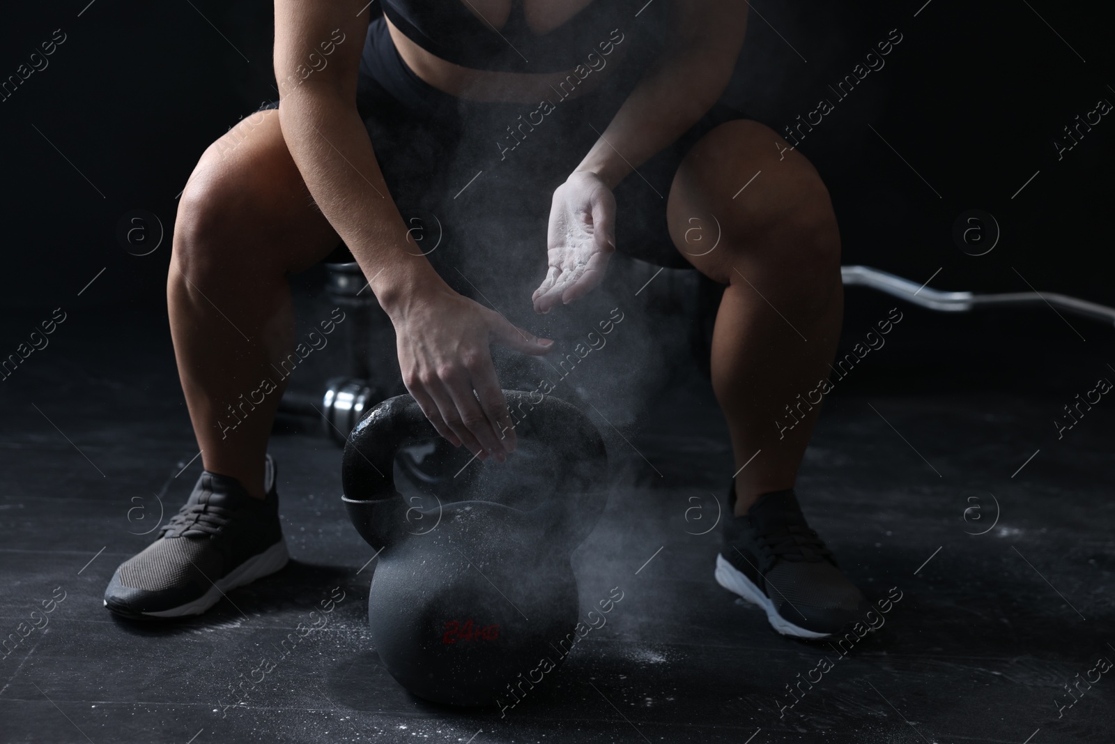 Photo of Woman with talcum powder on hands training with kettlebell against black background, closeup