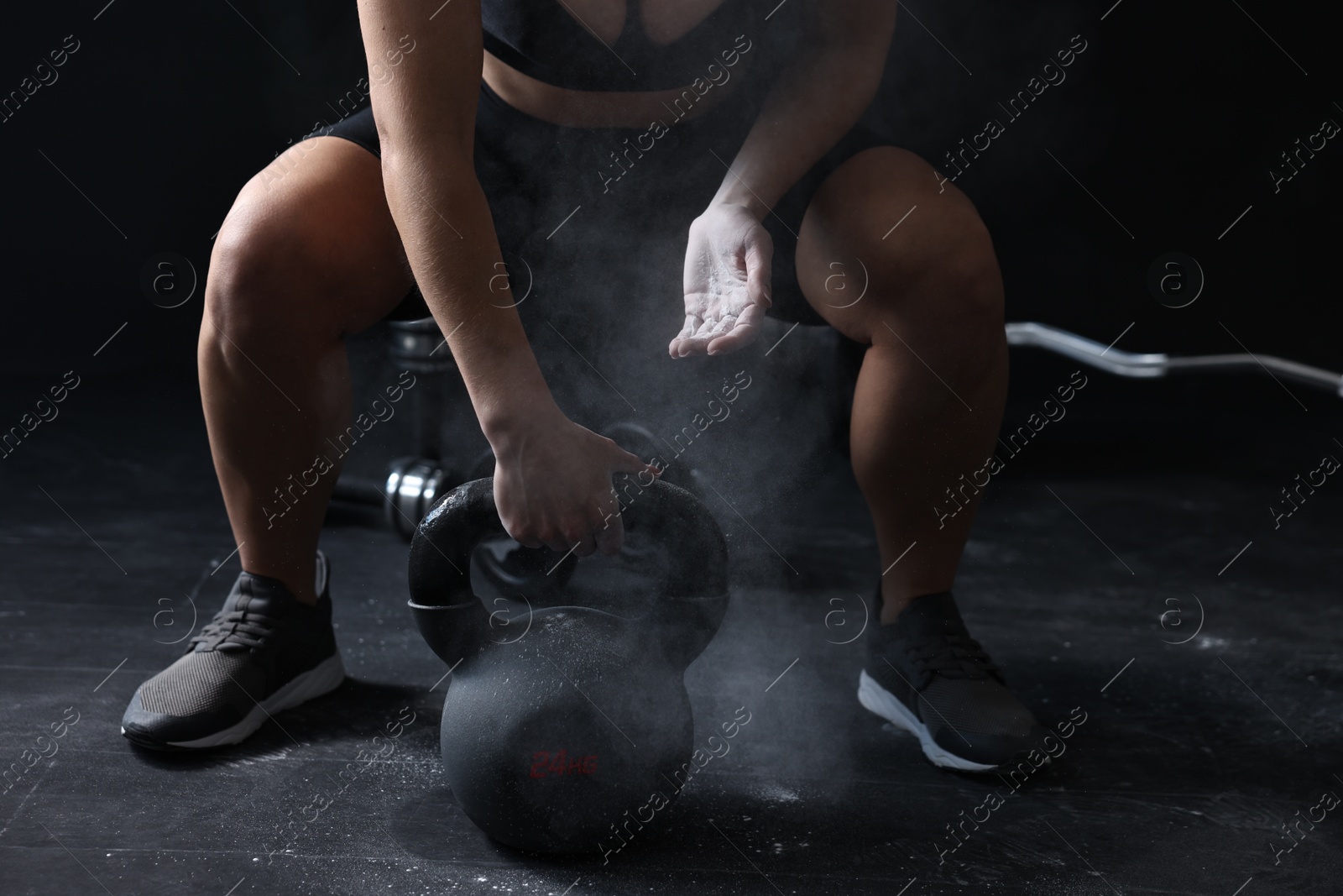 Photo of Woman with talcum powder on hands training with kettlebell against black background, closeup