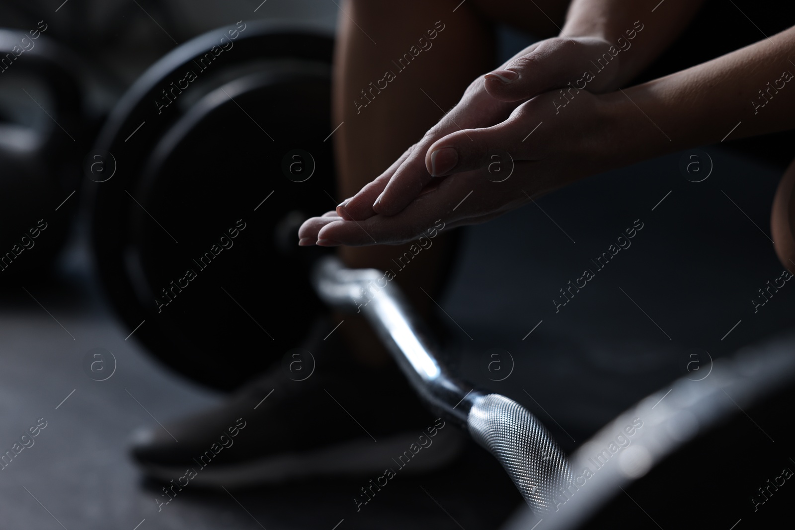 Photo of Woman clapping hands with talcum powder before training with barbell in gym, closeup