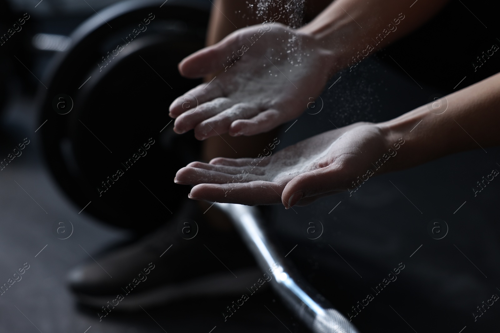 Photo of Woman with talcum powder on hands before training with barbell in gym, closeup