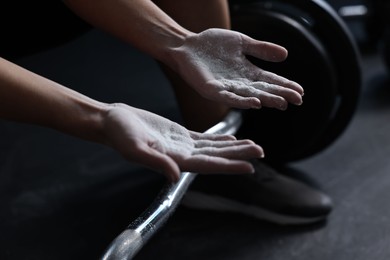 Photo of Woman with talcum powder on hands before training with barbell in gym, closeup