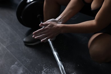 Photo of Woman clapping hands with talcum powder before training with barbell in gym, closeup