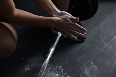 Photo of Woman clapping hands with talcum powder before training with barbell in gym, closeup