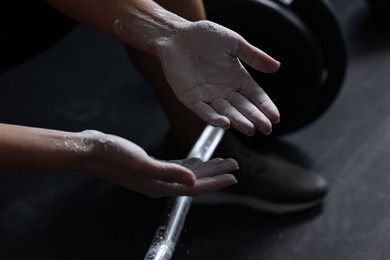 Photo of Woman with talcum powder on hands before training with barbell in gym, closeup