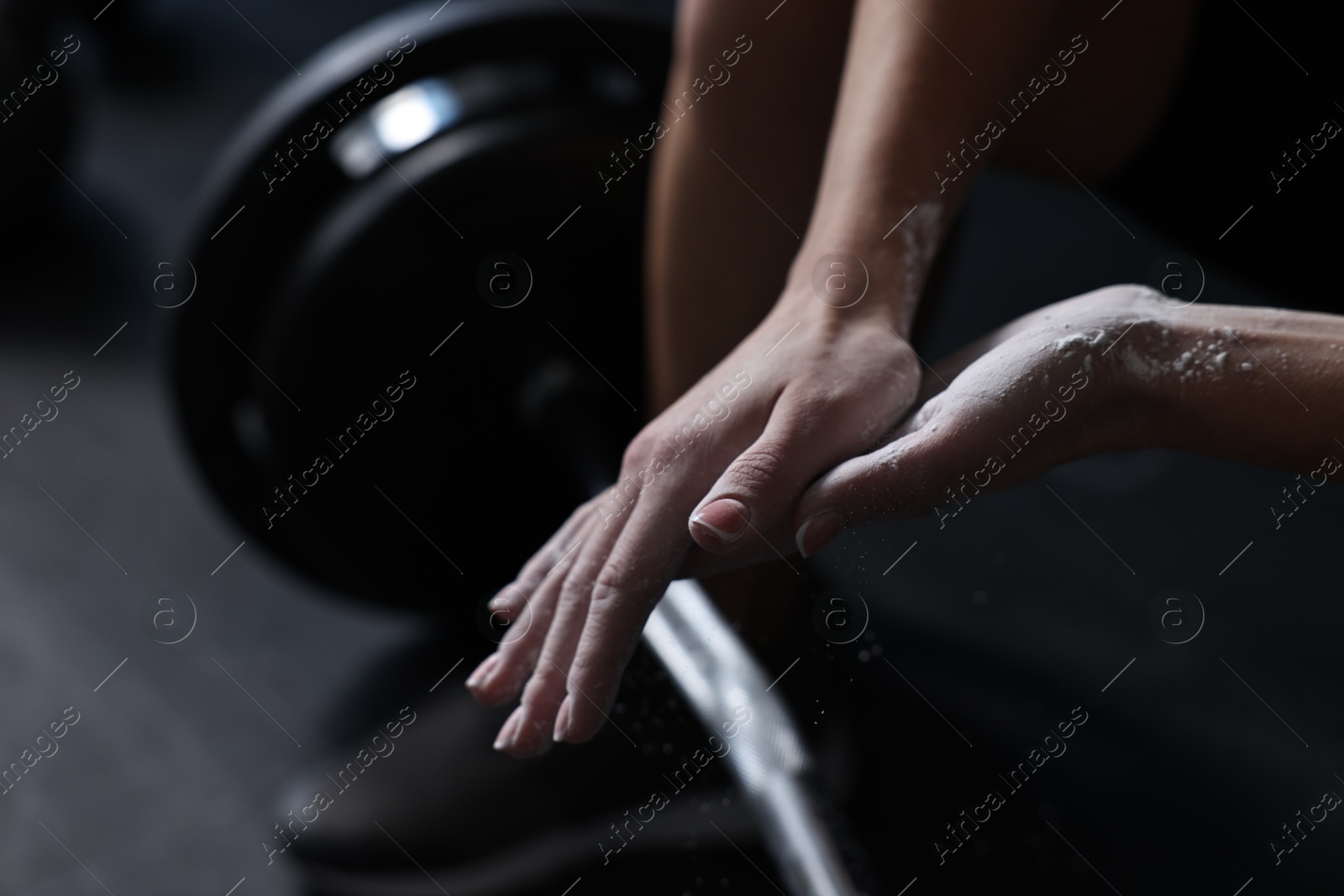 Photo of Woman applying talcum powder onto hands before training with barbell in gym, closeup