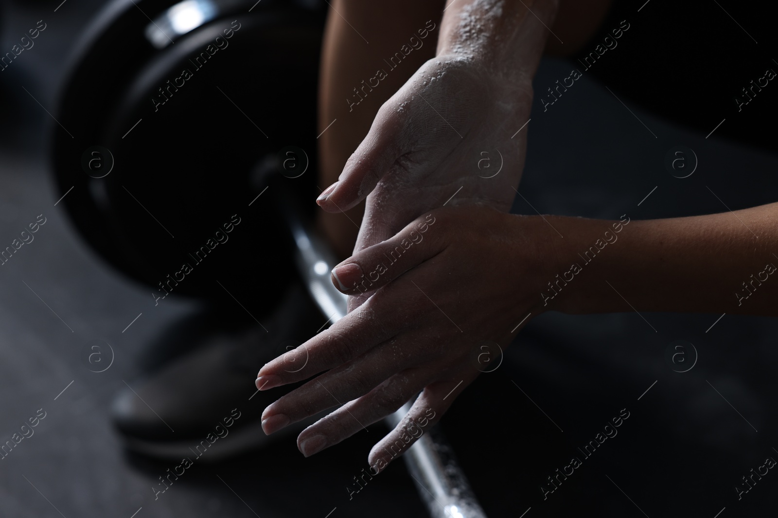 Photo of Woman applying talcum powder onto hands before training with barbell in gym, closeup