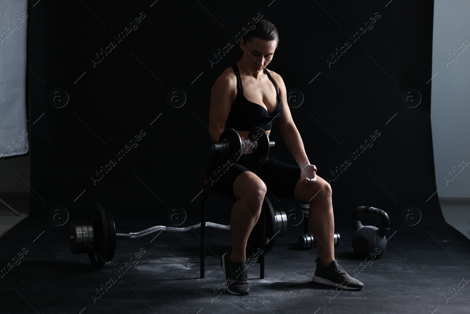 Photo of Woman with talcum powder on hands training with barbell against black background