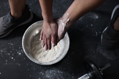 Photo of Woman applying talcum powder onto her hands above bowl before training in gym, top view