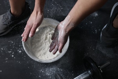 Photo of Woman applying talcum powder onto her hands above bowl before training in gym, top view