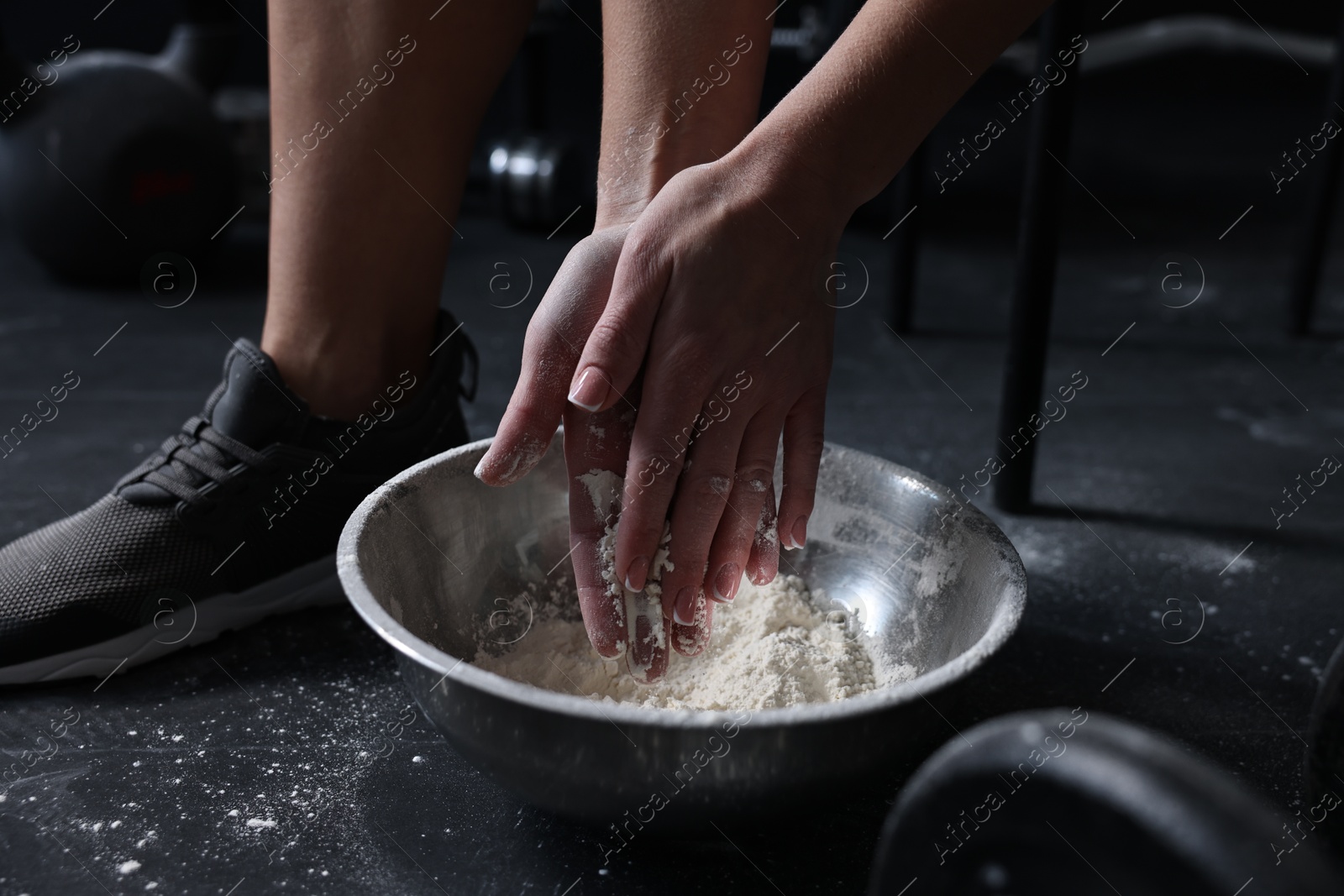 Photo of Woman applying talcum powder onto her hands above bowl before training in gym, closeup