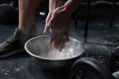 Photo of Woman applying talcum powder onto her hands above bowl before training in gym, closeup