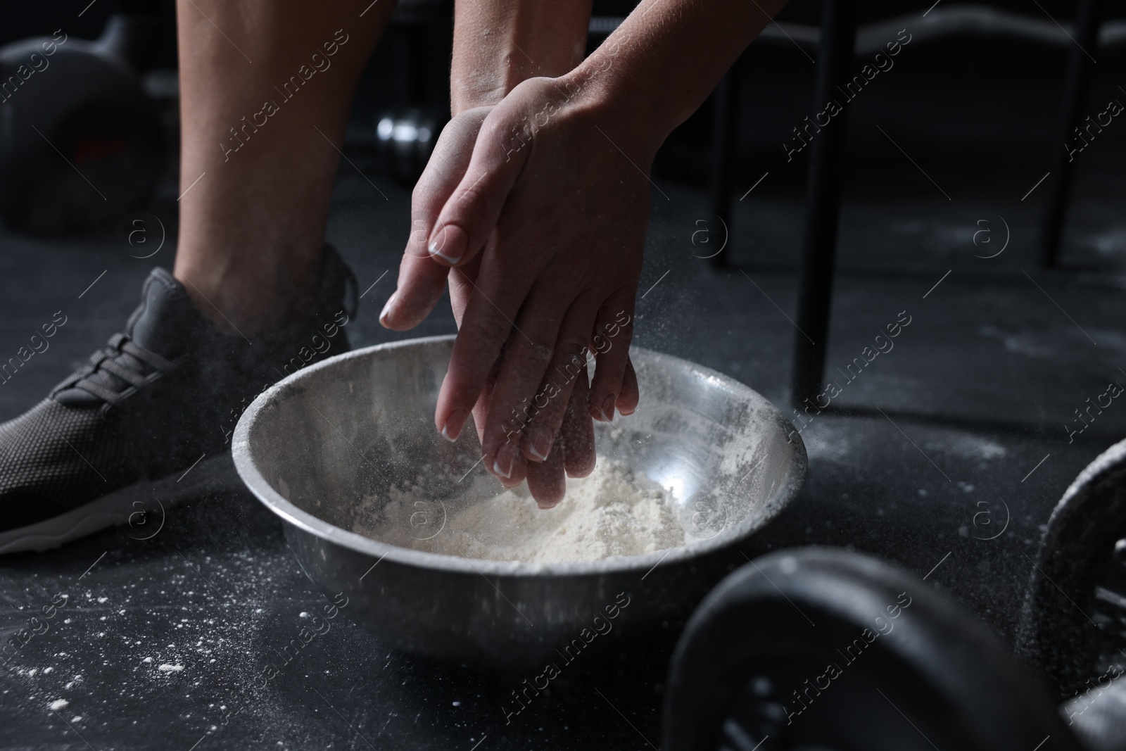 Photo of Woman applying talcum powder onto her hands above bowl before training in gym, closeup