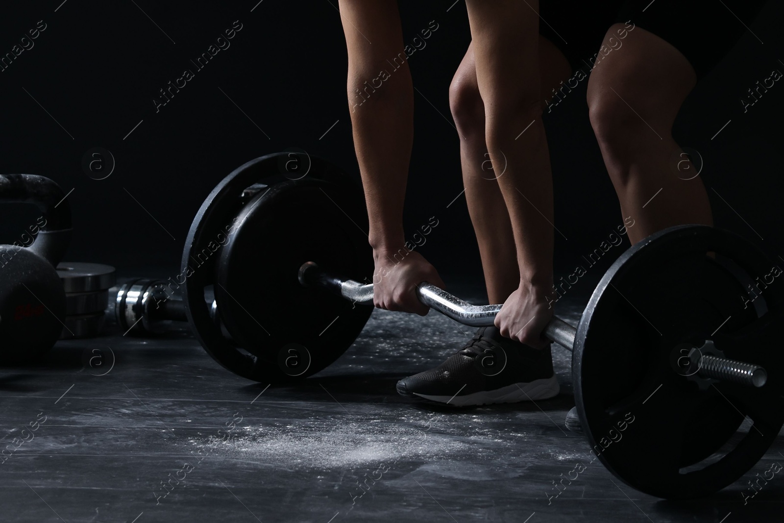 Photo of Woman with talcum powder on her hands training with barbell against black background, closeup