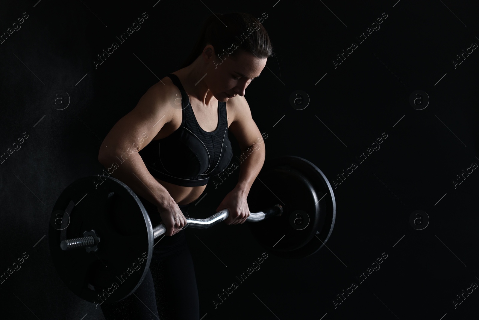 Photo of Woman training with barbell against black background