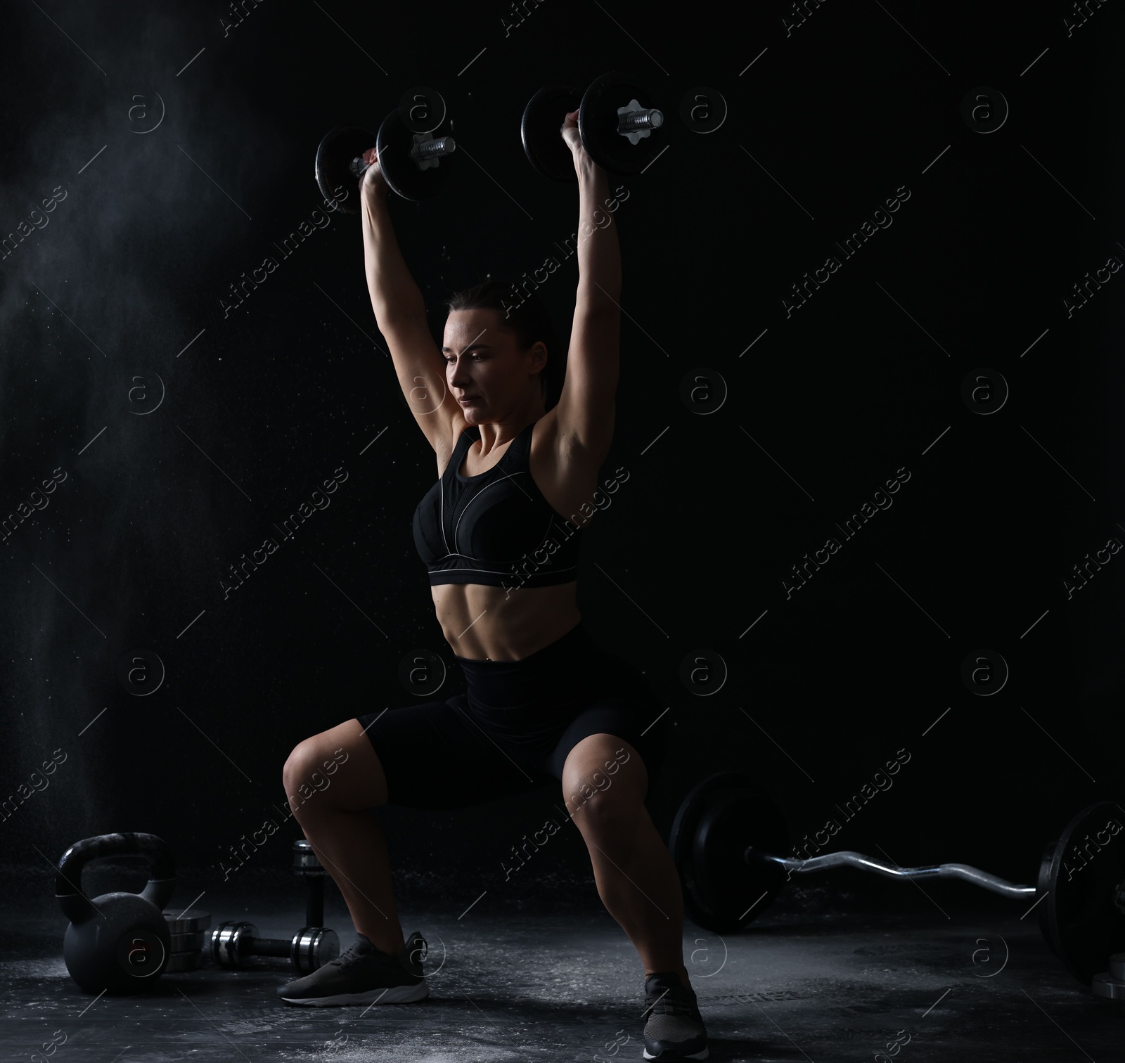 Photo of Woman training with barbells on black background