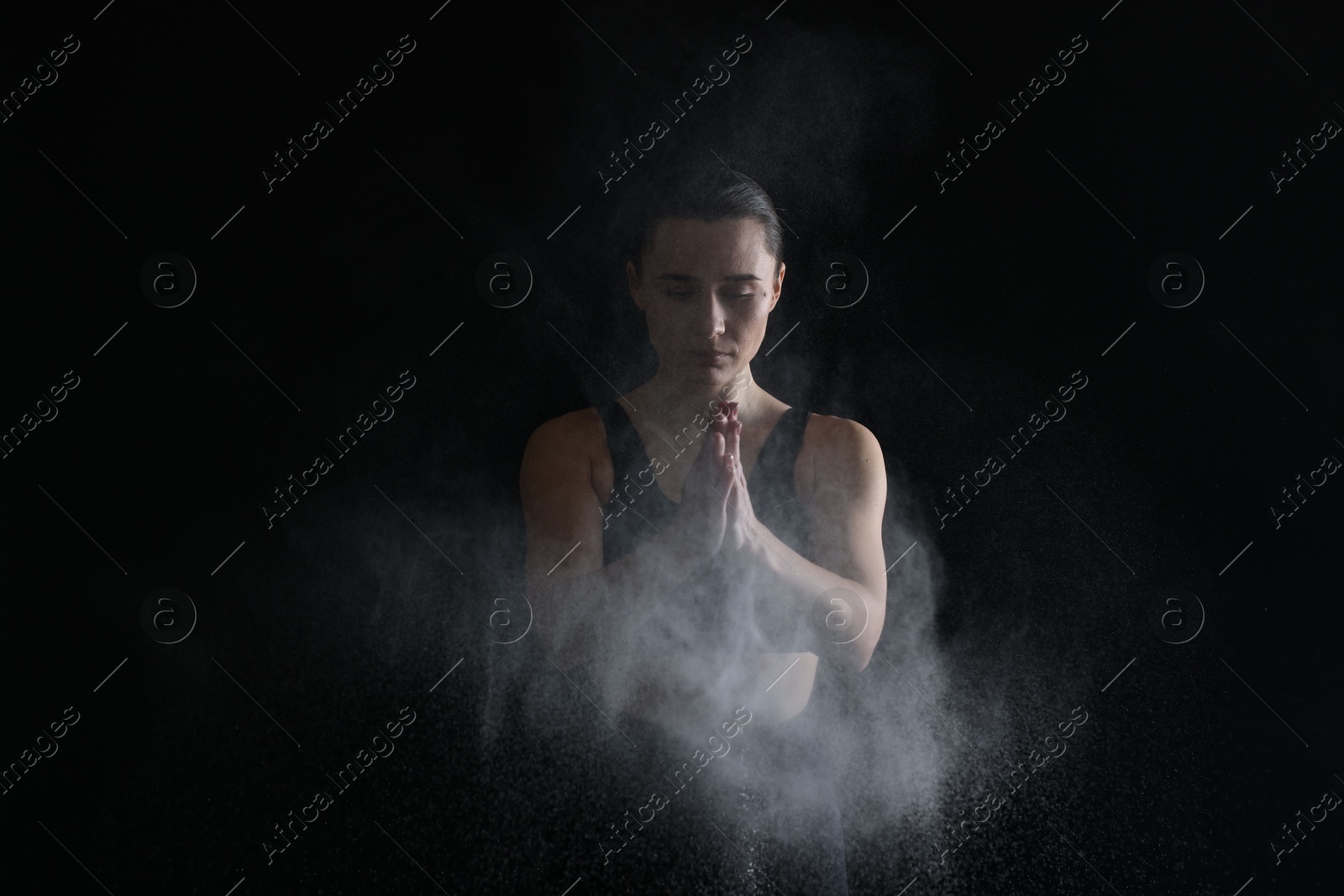 Photo of Woman clapping hands with talcum powder before training on black background