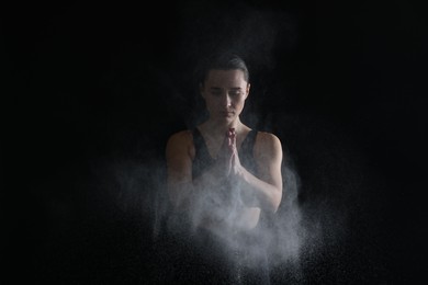 Photo of Woman clapping hands with talcum powder before training on black background