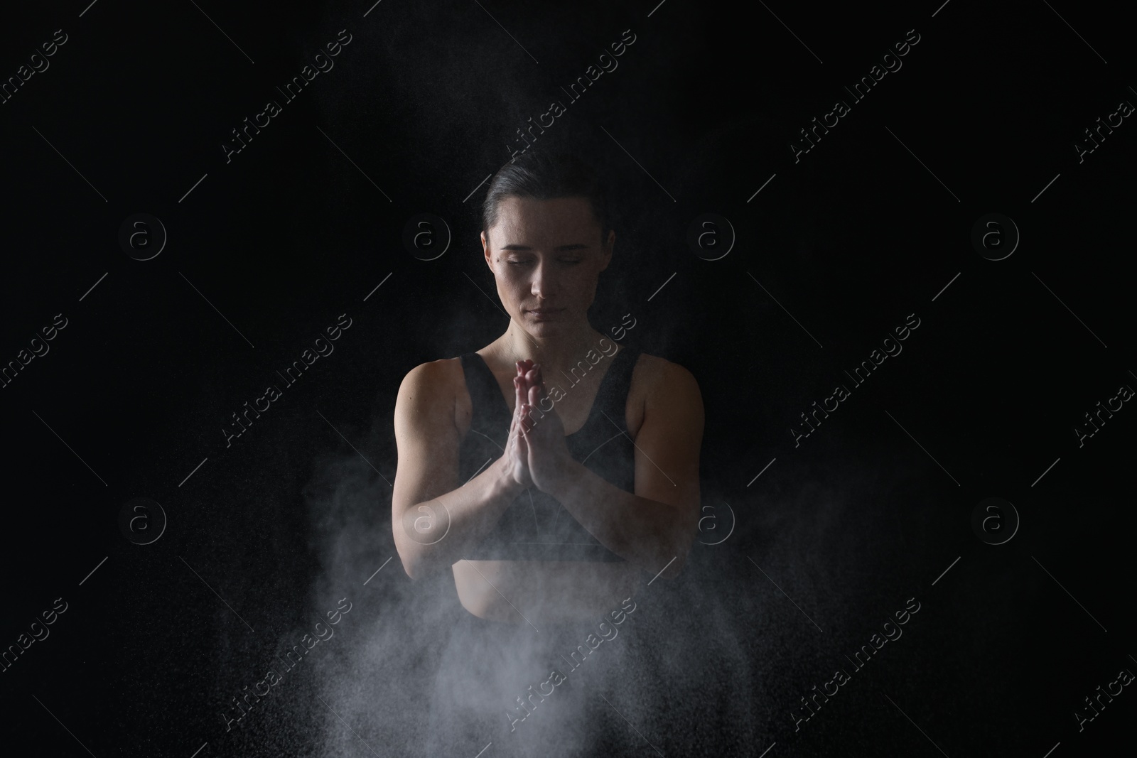 Photo of Woman clapping hands with talcum powder before training on black background