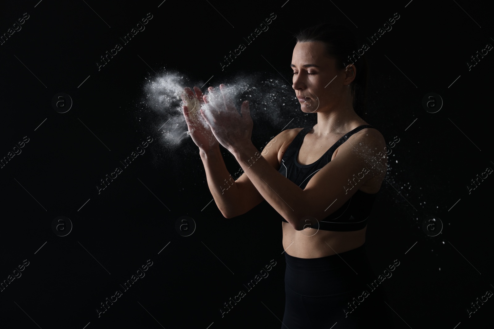 Photo of Woman clapping hands with talcum powder before training on black background. Space for text