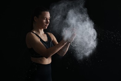 Photo of Woman clapping hands with talcum powder before training on black background