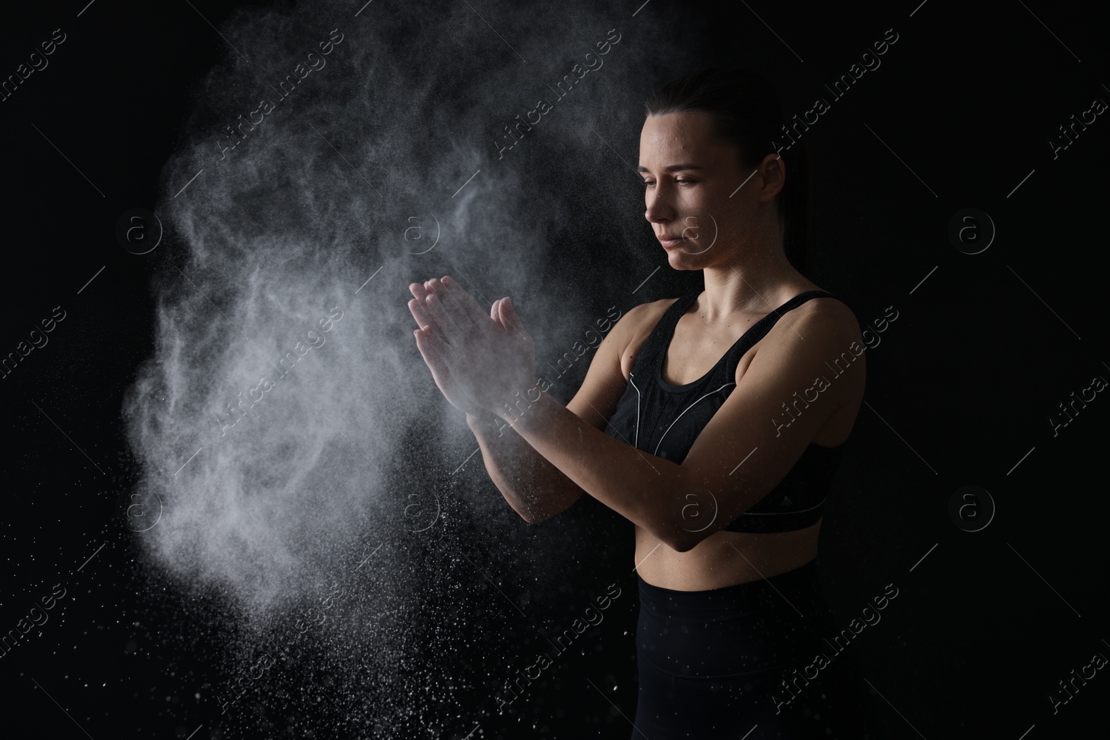 Photo of Woman clapping hands with talcum powder before training on black background