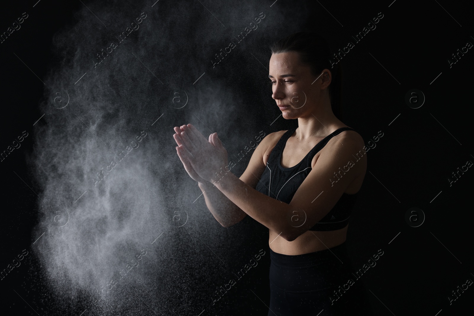 Photo of Woman clapping hands with talcum powder before training on black background