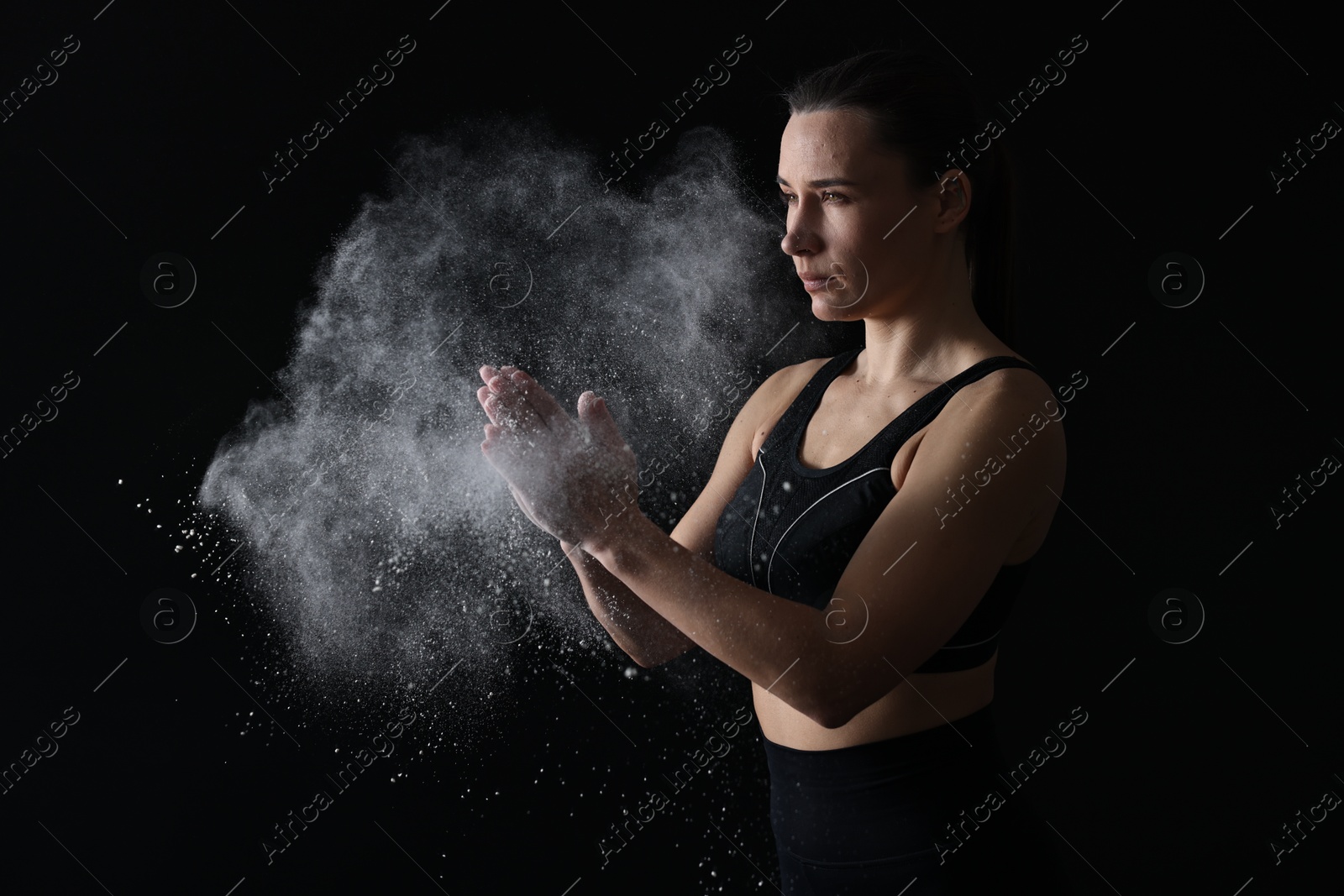 Photo of Woman clapping hands with talcum powder before training on black background