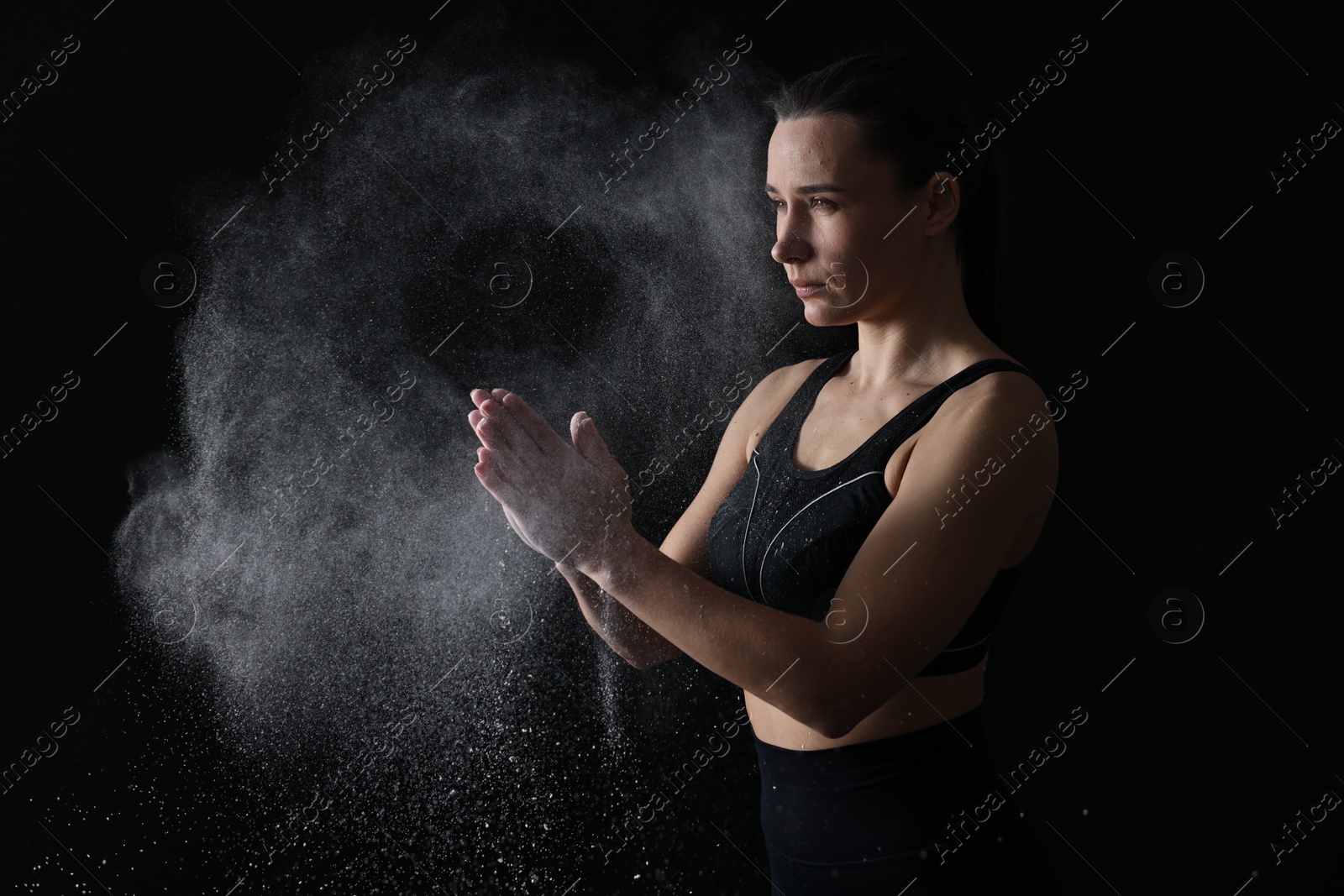 Photo of Woman clapping hands with talcum powder before training on black background