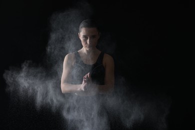 Photo of Woman clapping hands with talcum powder before training on black background