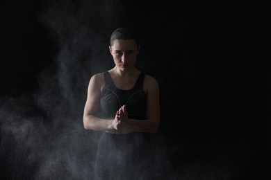 Photo of Woman clapping hands with talcum powder before training on black background