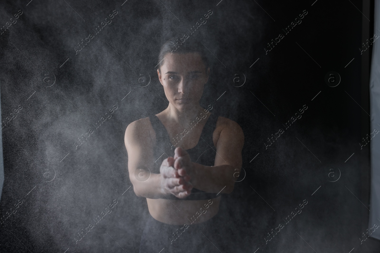 Photo of Woman clapping hands with talcum powder before training on black background