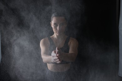 Photo of Woman clapping hands with talcum powder before training on black background