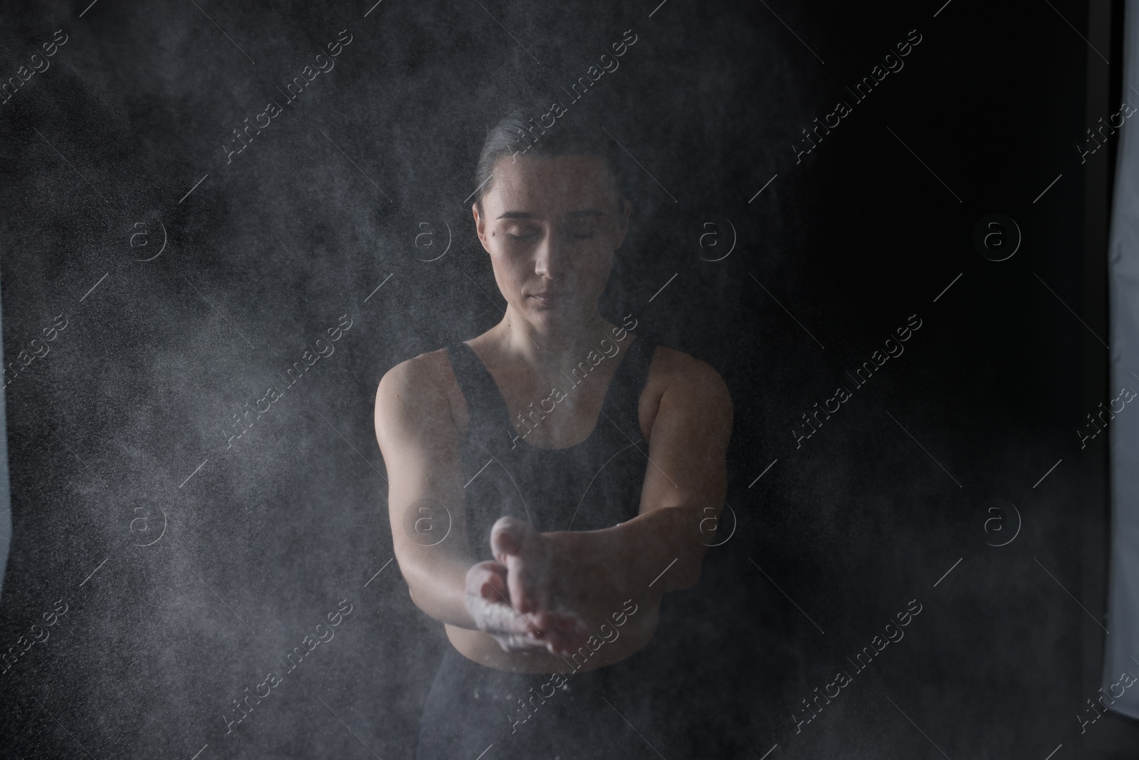 Photo of Woman clapping hands with talcum powder before training on black background