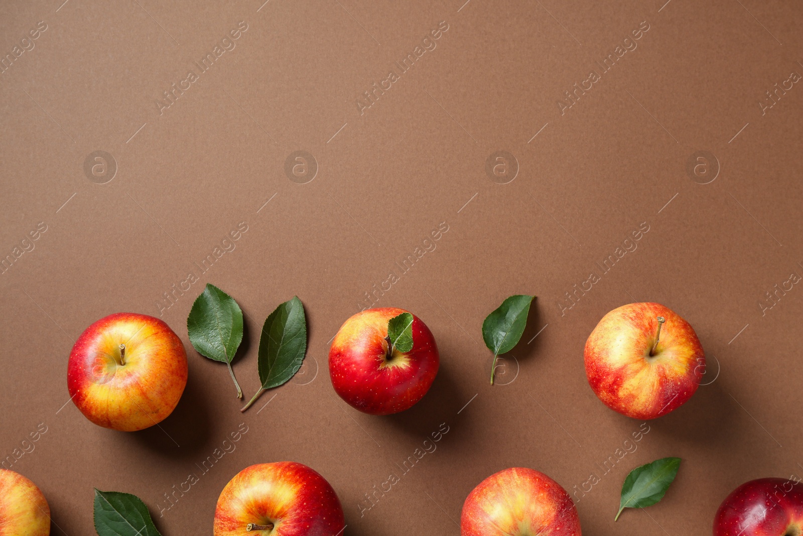 Photo of Ripe red apples and green leaves on brown background, flat lay. Space for text