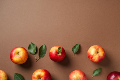 Ripe red apples and green leaves on brown background, flat lay. Space for text