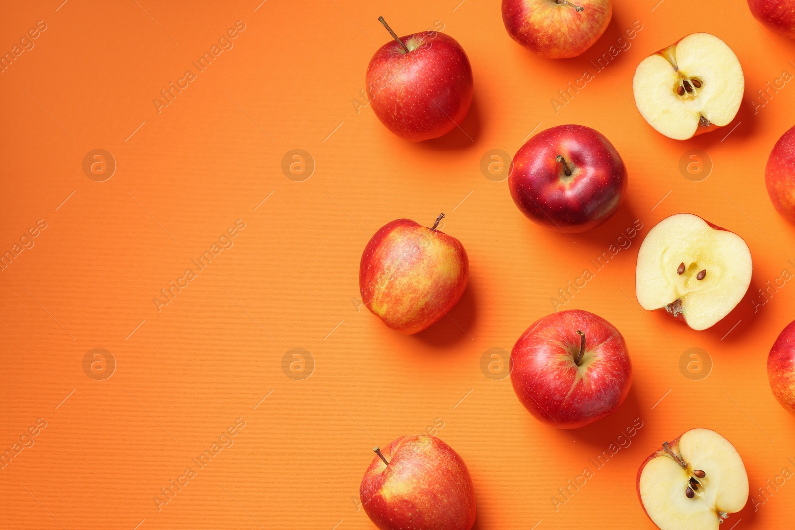 Photo of Whole and cut fresh red apples on orange background, flat lay. Space for text