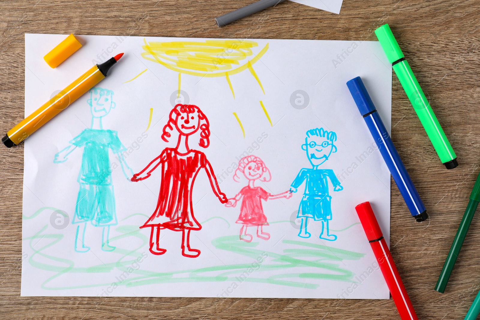 Photo of Child's drawing of happy family and felt tip pens on wooden table, top view