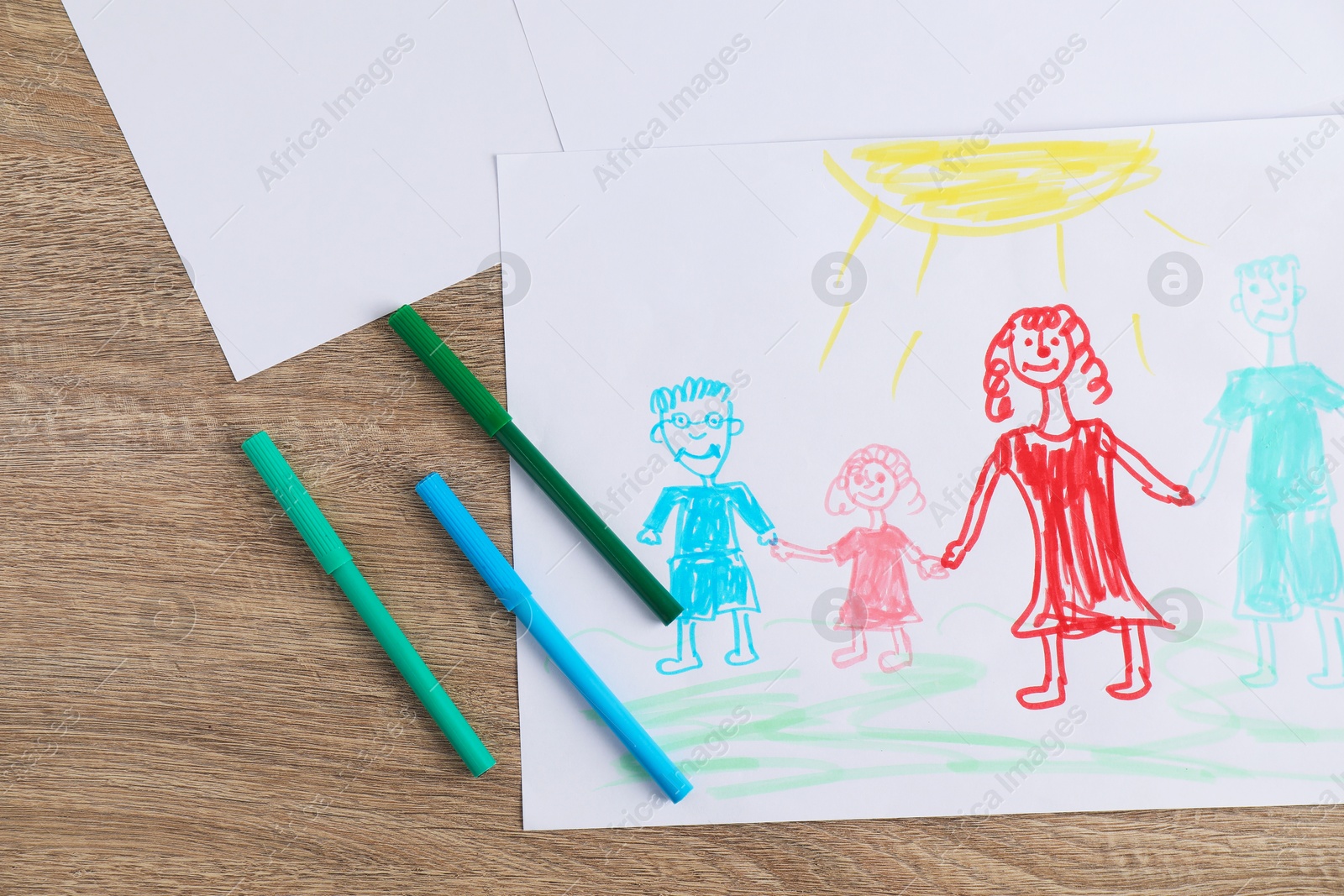 Photo of Child's drawing of happy family and felt tip pens on wooden table, top view