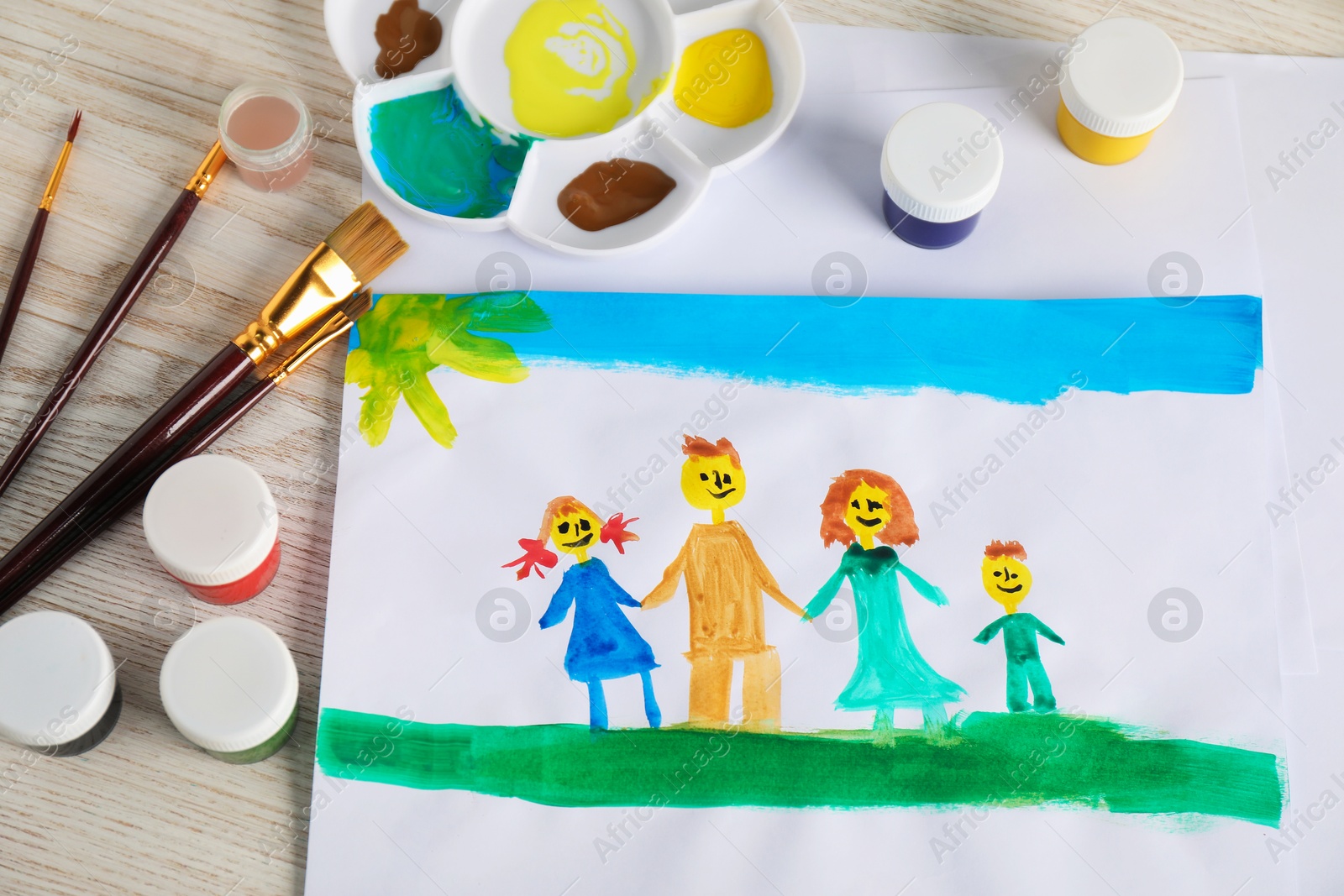 Photo of Child's drawing of happy family and supplies on wooden table, top view