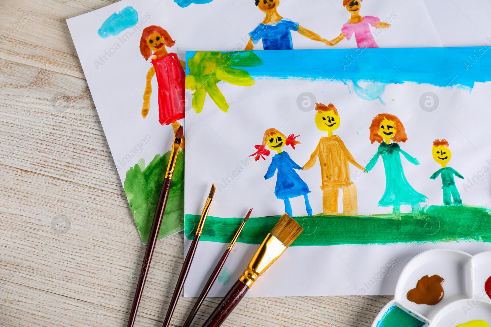 Photo of Child's drawing of happy family and supplies on wooden table, top view