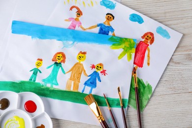 Photo of Child's drawing of happy family and supplies on wooden table, top view