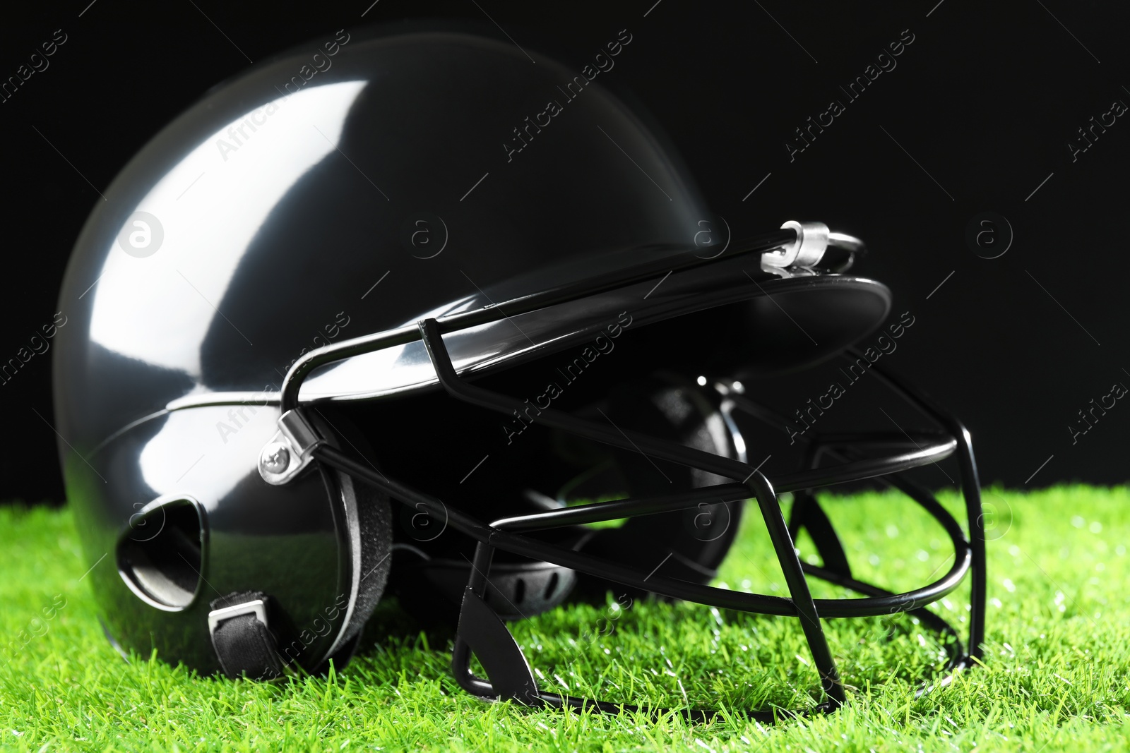 Photo of Baseball helmet on artificial grass against black background, closeup