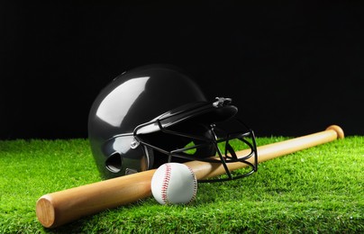 Photo of Baseball helmet, bat and ball on artificial grass against black background