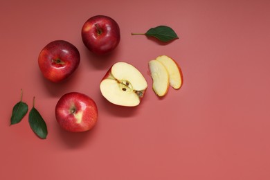 Fresh apples and green leaves on red background, flat lay. Space for text