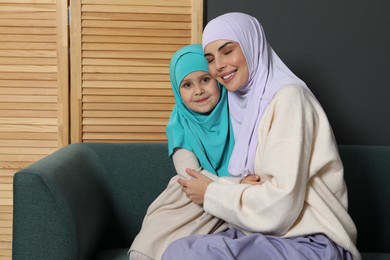 Photo of Muslim woman and her daughter sitting on sofa at home