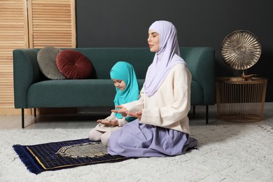 Photo of Muslim woman and her daughter praying on mat at home