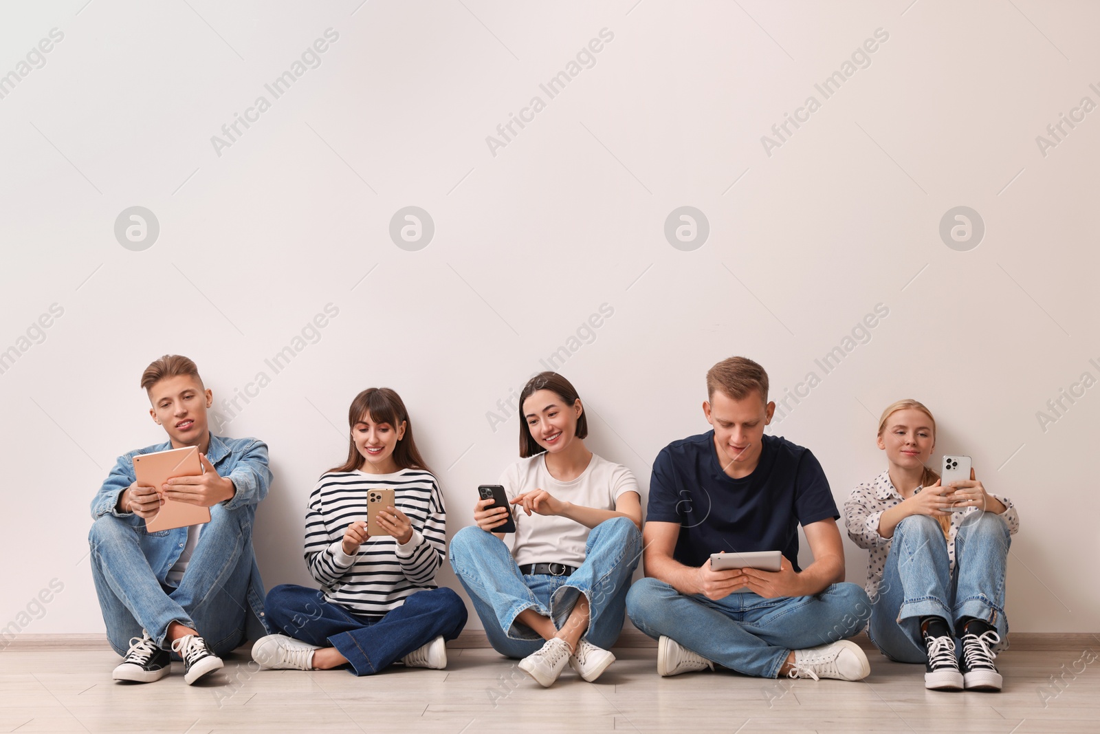 Photo of Group of people using different gadgets near white wall indoors. Modern technology